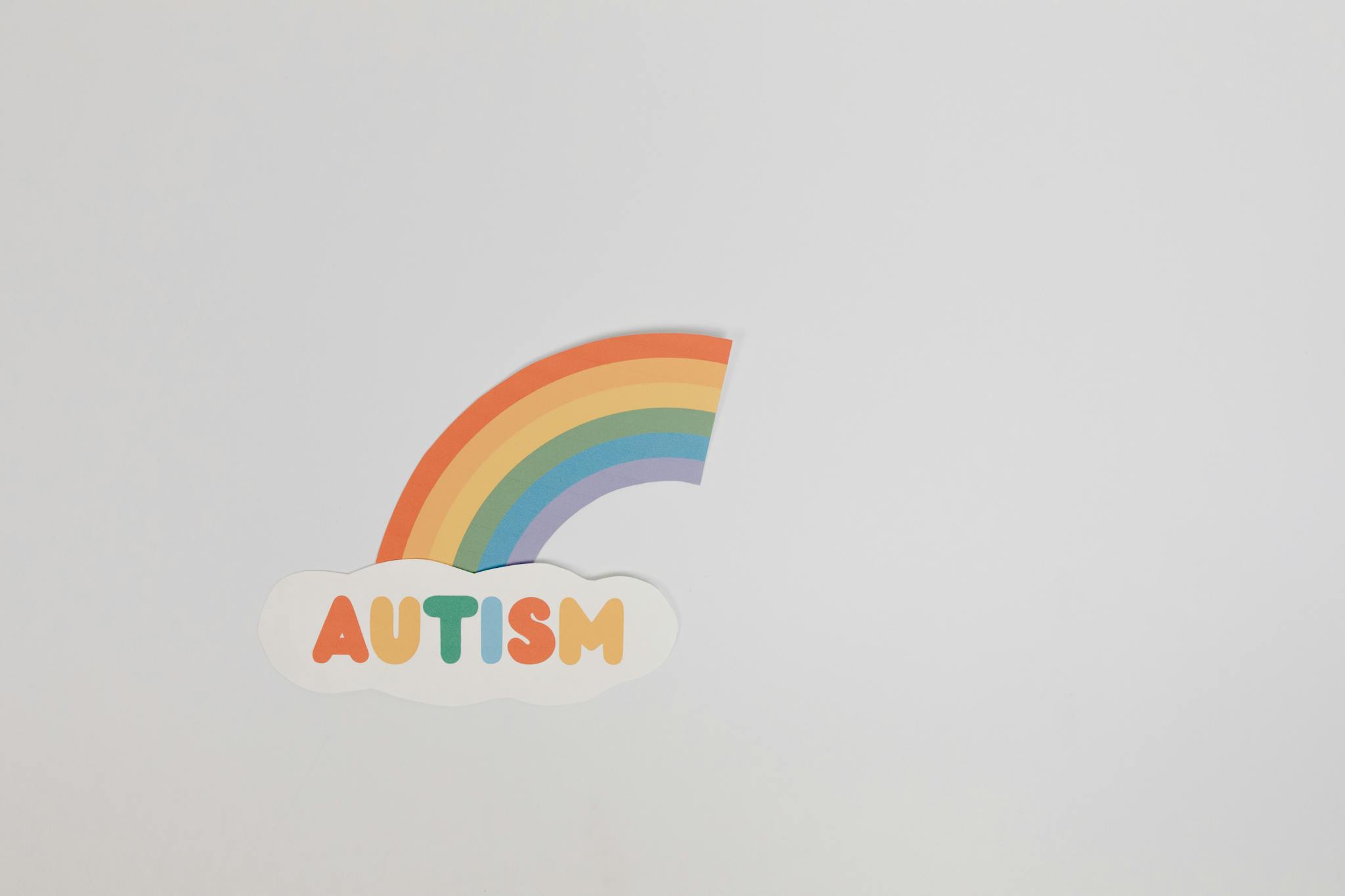 A colorful rainbow above the word 'AUTISM' on a minimalist white background, symbolizing autism awareness.