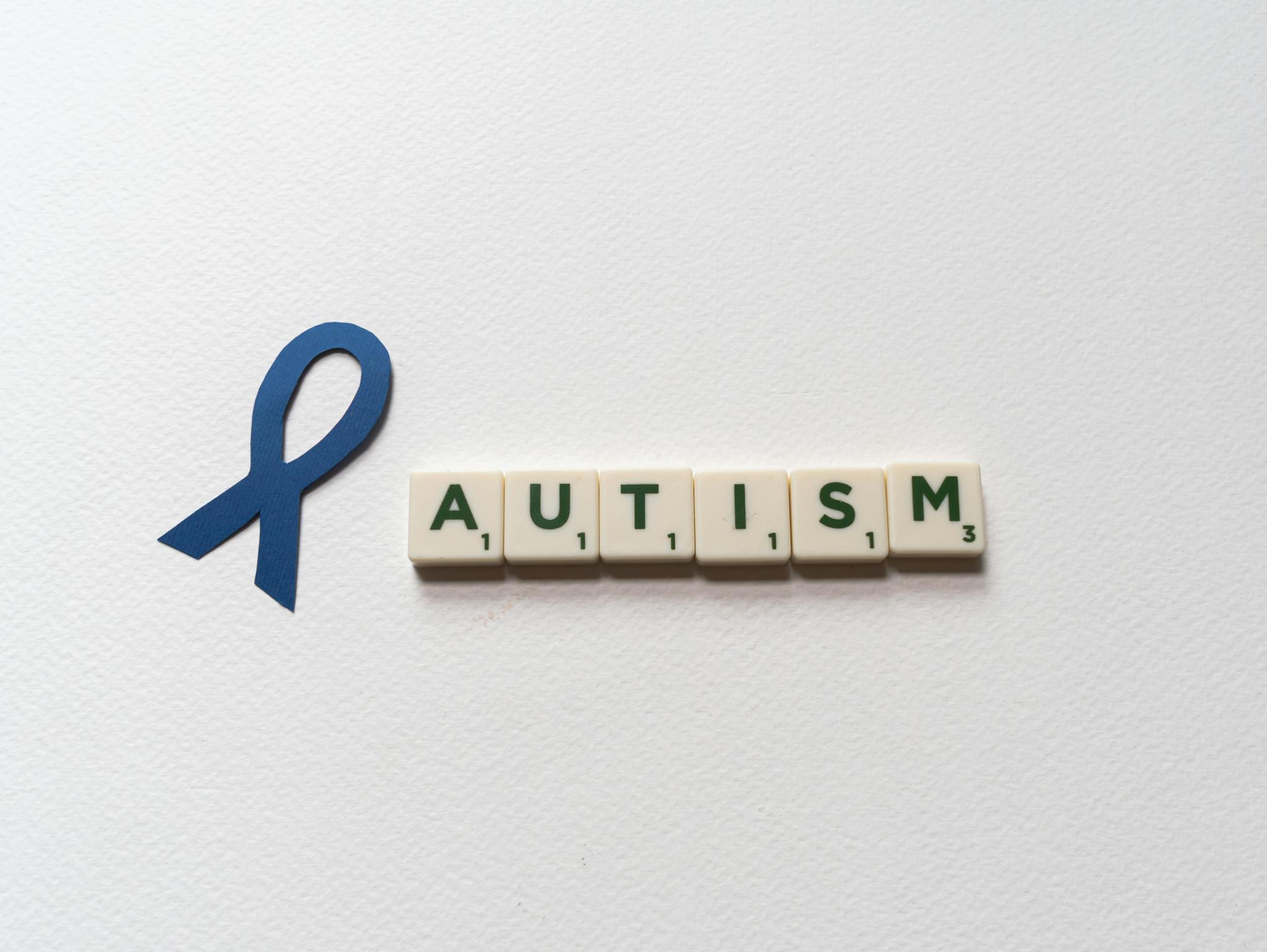 Blue ribbon and autism spelled with letter tiles symbolize autism awareness.