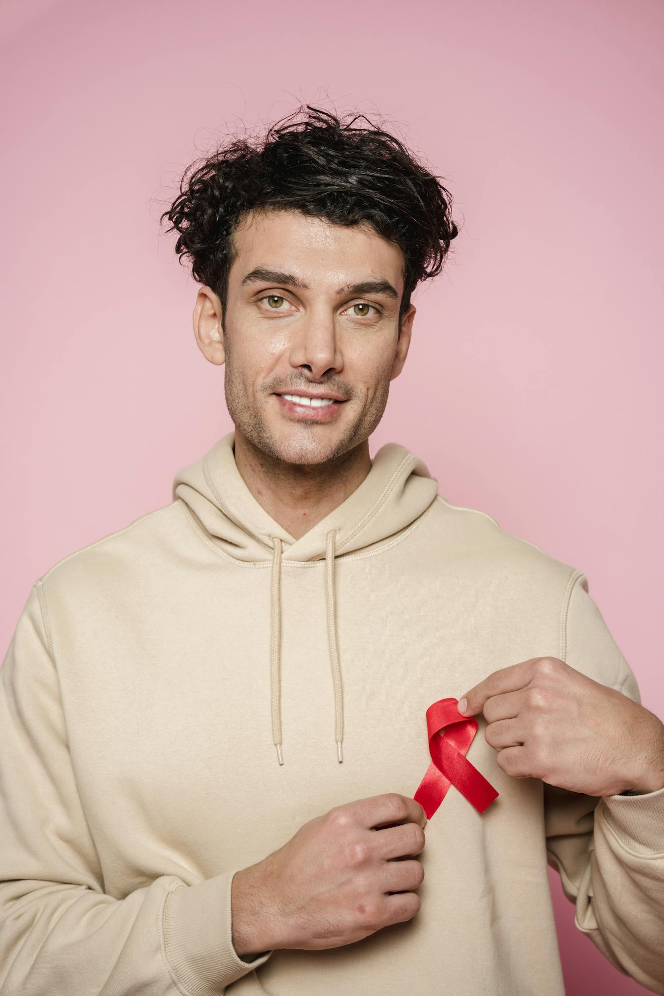 Portrait of a man holding a red awareness ribbon against a pink background, promoting health and support.